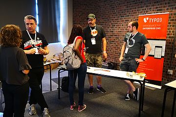 Groups of people in conversation with TYPO3-branded roll-up in the background.