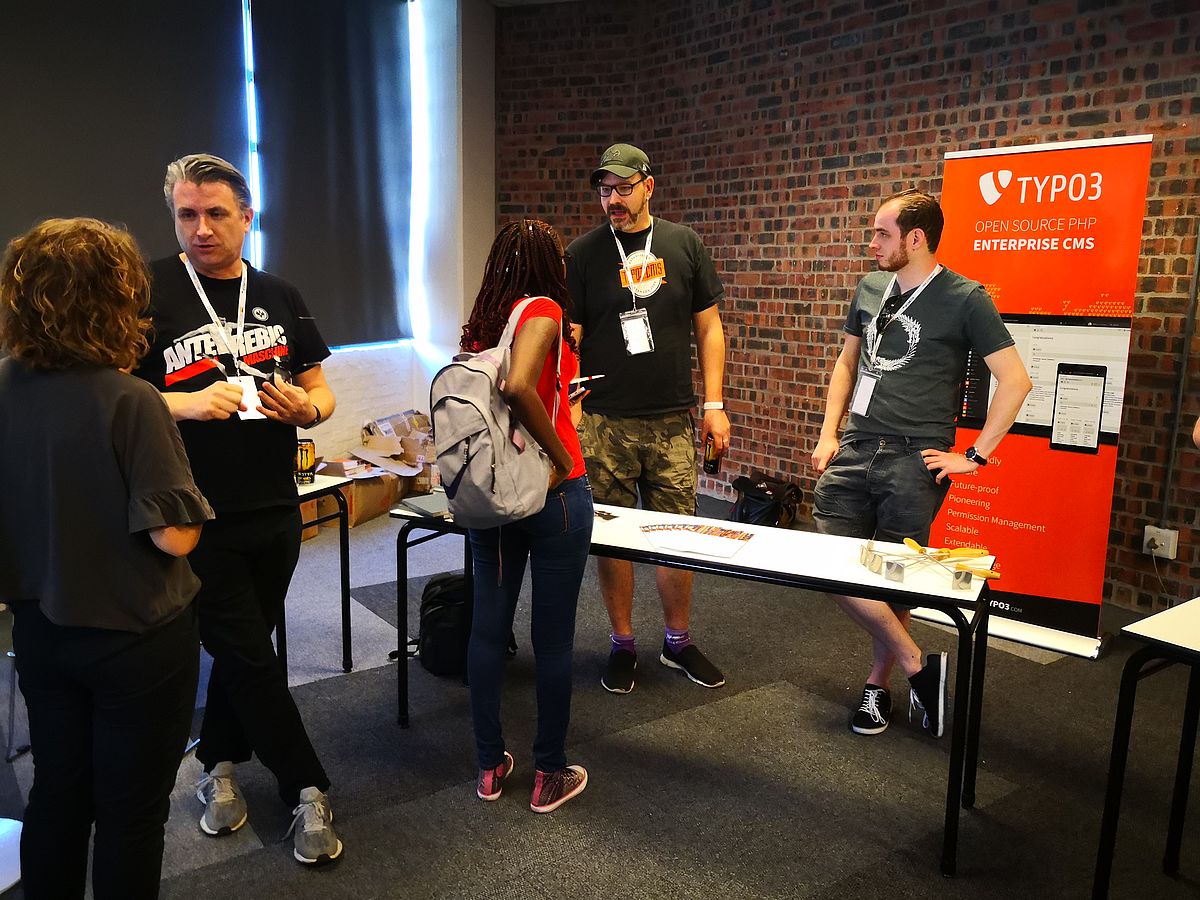 Groups of people in conversation with TYPO3-branded roll-up in the background.