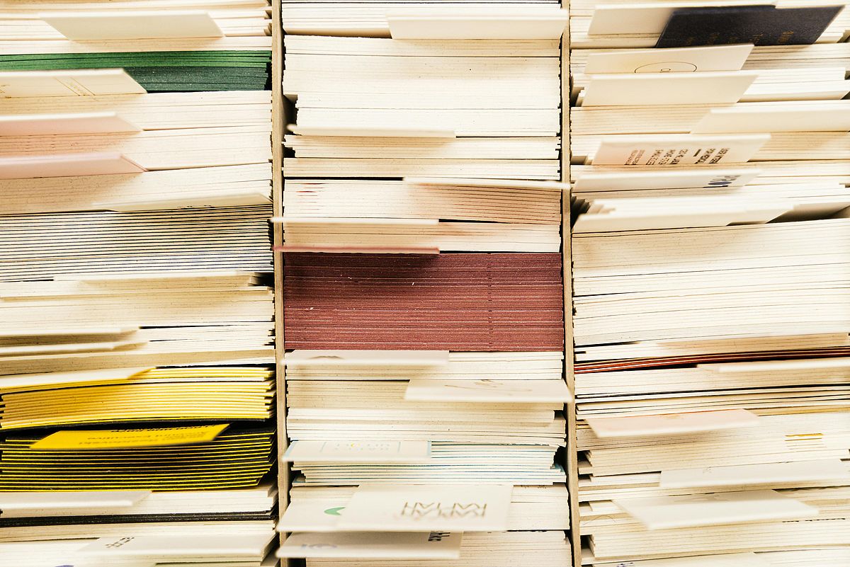 Stacks of various colorful paper files and documents, densely packed and organized on shelves, creating a visually textured pattern with edges visible, and some paper edges showing different colors like yellow, red, and green.