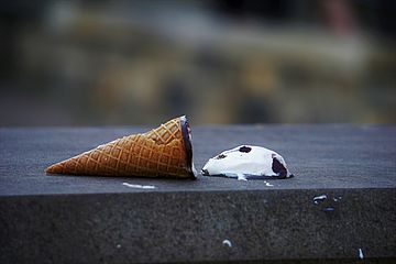 Ice cream cone lying on its side with ice cream spilling out of it.
