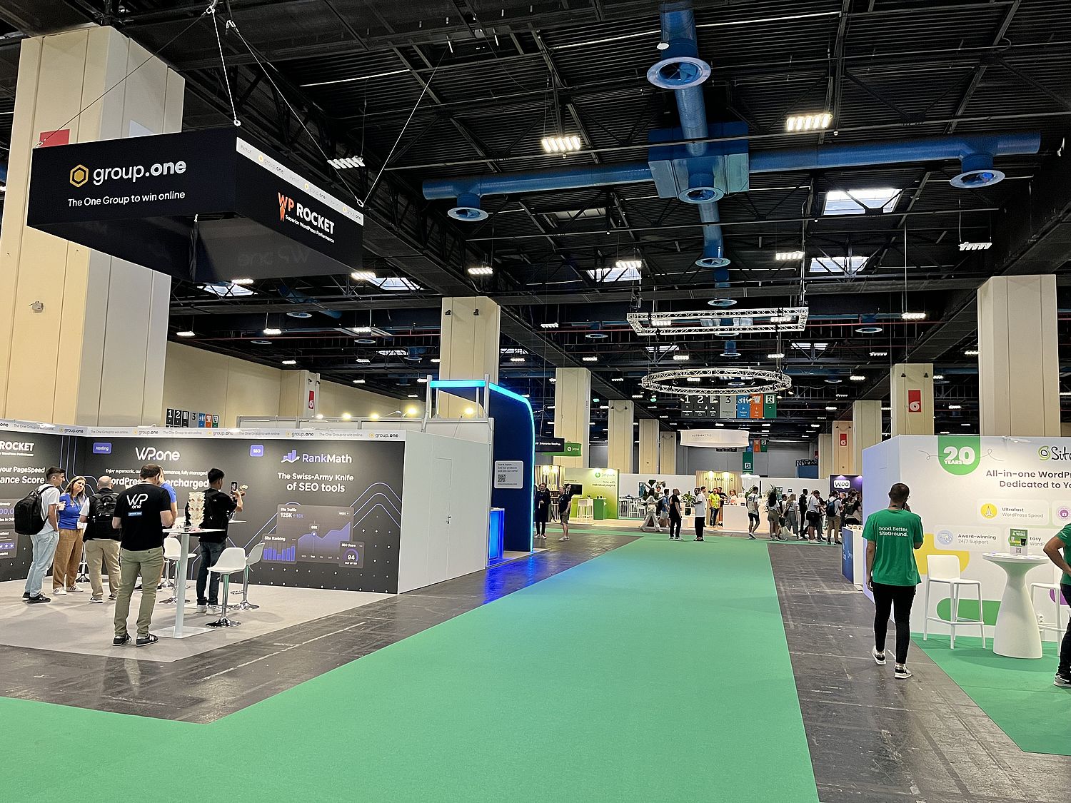 A large exhibition hall with booths on each side of a green floor.