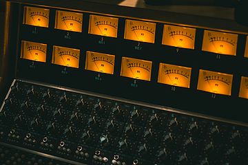Audio mixer with analog volume unit meters lit with yellow light.