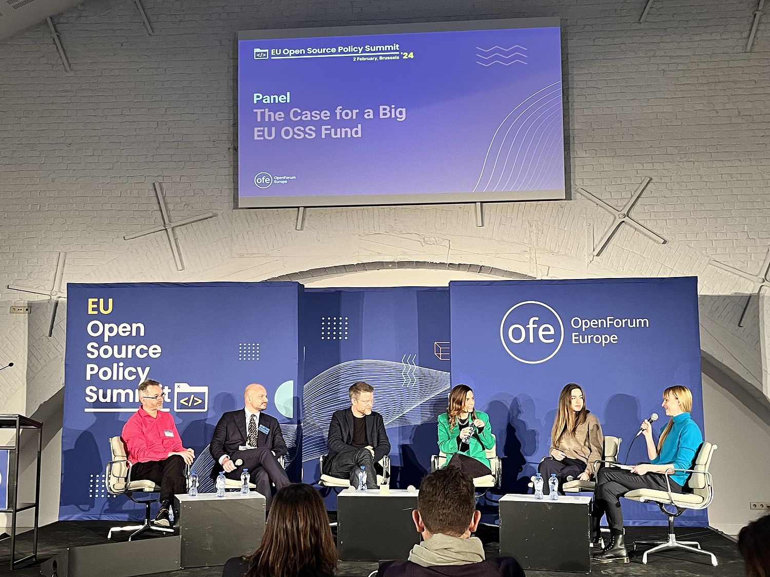Podium discussion with six participants, under a projection screen with the podium title: The Case for a Big EU OSS Fund