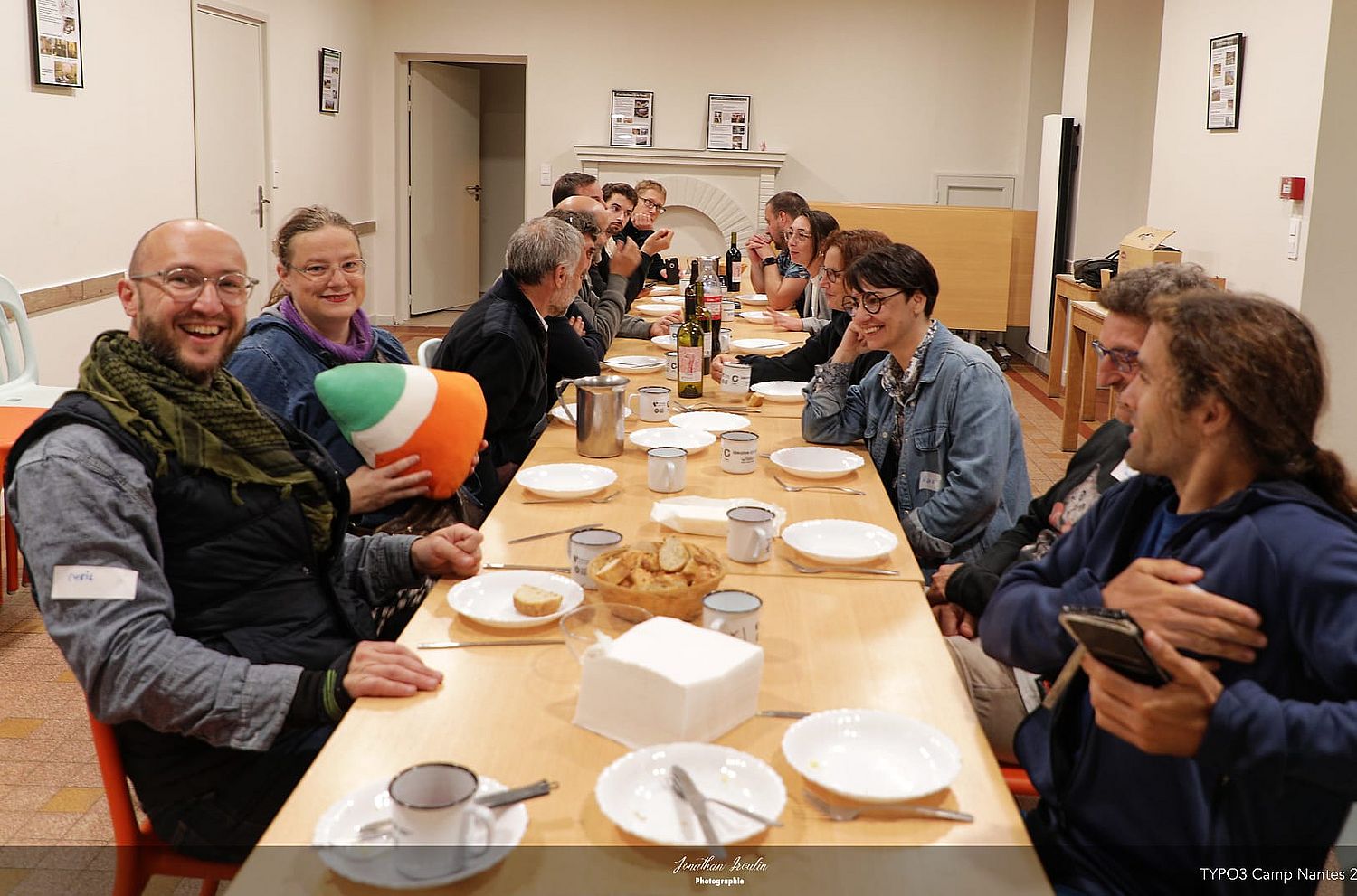 People at mealtime, smiling. A long table with empty white plates.