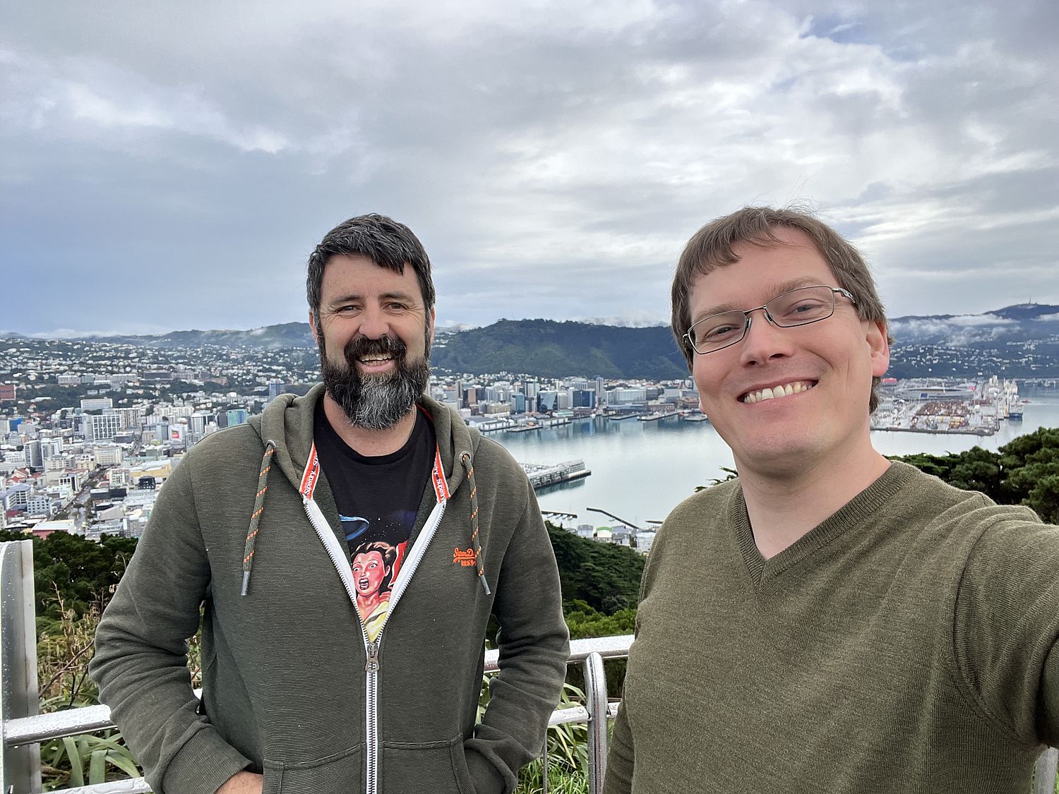 Photo of two men, smiling, with a city in the background.