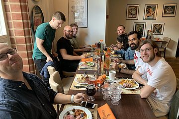 View down a long table with food in a restaurant. People seated and looking at the camera.