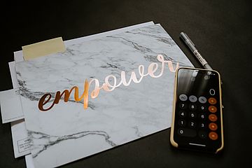 Sheet of paper with the word "empower" in golden writing next to a calculator.