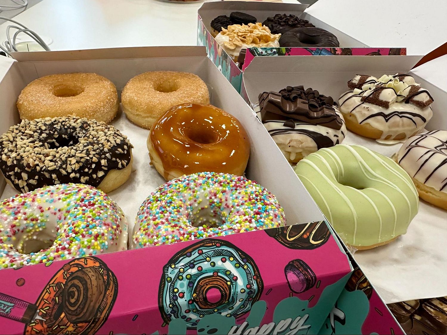 Donuts of different colors in paper boxes.