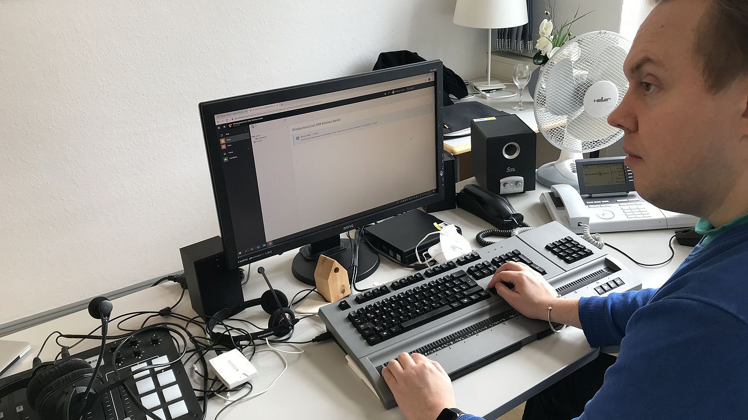 Matthias Henke sitting at a desk with a monitor and a keyboard with built-in Braille display. The monitor shows the TYPO3 Backend.