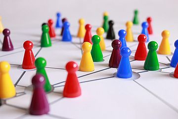 Multicolored game pieces arranged on a white surface, connected by lines to illustrate a network. The pieces are placed at intersections, symbolizing connections and interactions within the network.