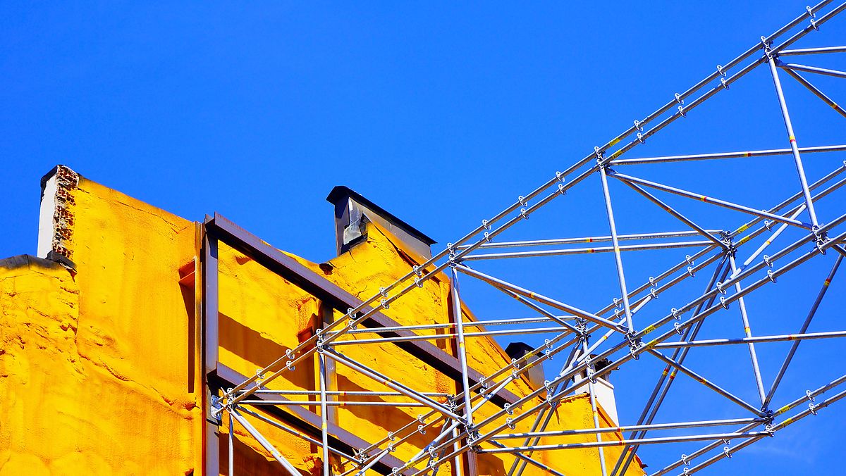Gray metal construction frame next to a yellow brick wall.