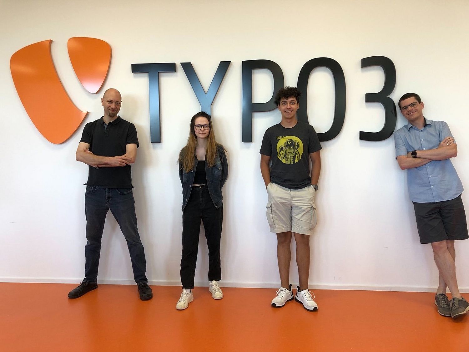 Four people in front of a white wall with the TYPO3 logo.