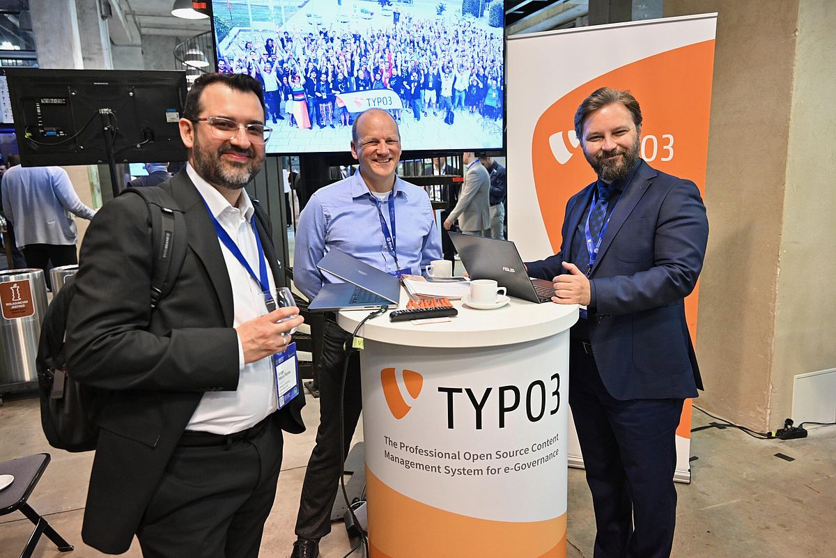 Three people standing around a TYPO3-branded booth table.