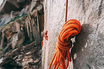 A partially curled-up red climbing rope hanging down a steep rock face.