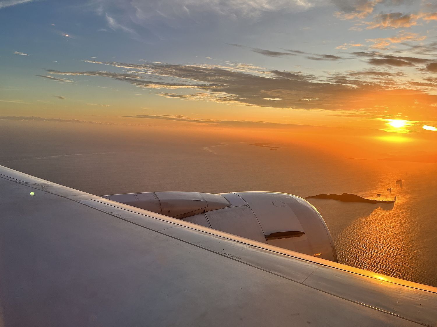 Ocean sunset with islands seen over an airplane wing with jet engine.