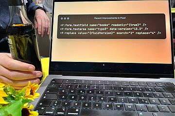 A laptop screen showing a code example. Next to it, a bottle of a black liquid and a bouquet of flowers.