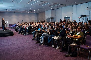 A conference hall full of people. A speaker on a podium.