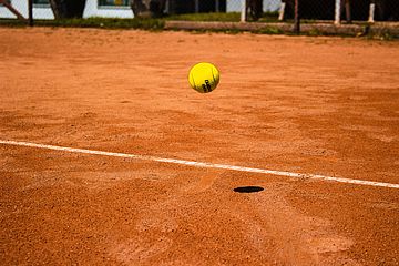 Yellow tennis ball hovering over orange sand.