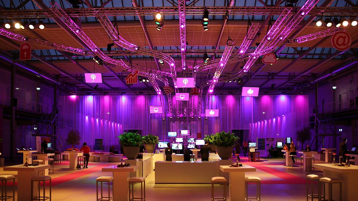 Large hall with high tables and stools spread about in magenta light.