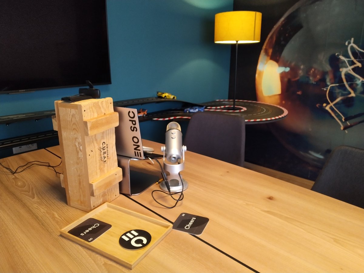 Wooden table with microphone and laptop. Toy car racing track in the background.