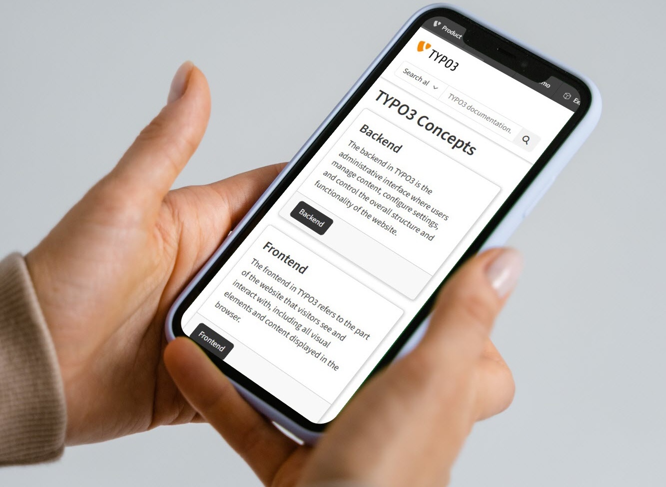 A person holds a smartphone displaying a webpage about TYPO3 Concepts with sections titled Backend and Frontend. The screen shows descriptions for both sections, and the person is using their left thumb to interact with the screen.